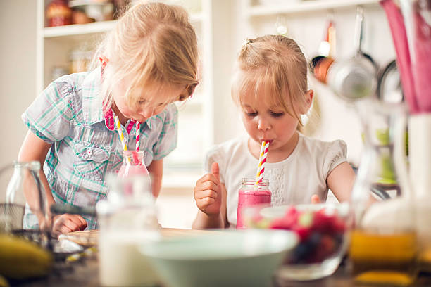 zwei kleine mädchen trinken frische smoothie - child jumping vegetable food stock-fotos und bilder