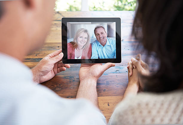 Tech that helps them to stay connected Shot of a married couple video calling family using their digital tablet over the shoulder view photos stock pictures, royalty-free photos & images