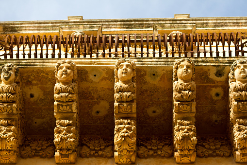 Noto, Sicily: An ornate baroque carved balcony (close-up). Baroque Southeast Sicily is known for its ornate exterior carvings, created in the early 18th century and made of the local sandstone. Noto is a UNESCO World Heritage site.