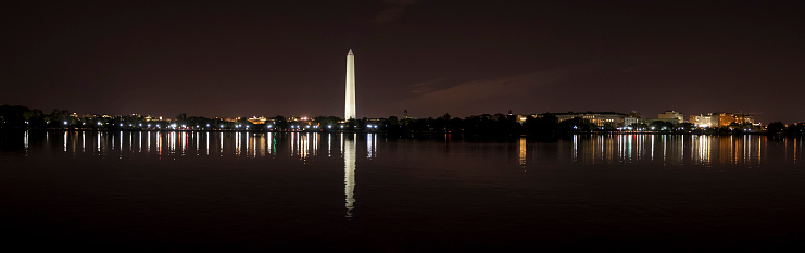 A panoramic night scene looking of the Washington Monument area with reflections in the water. This is a composite of multiple images.
