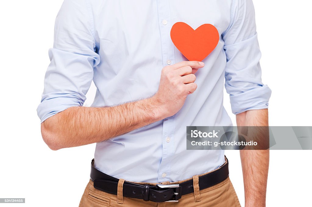 I am in love! Close-up of young man holding heart shaped valentine card in front of his heart while standing isolated on white background 2015 Stock Photo