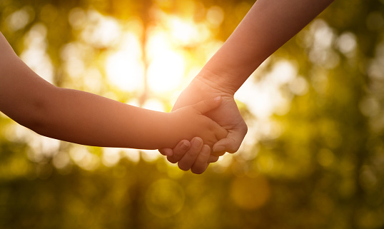 Close up of mother or older sister and a child hands at the sunset