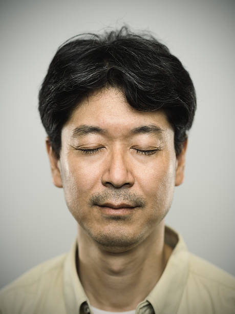Studio portrait of a japanese mature with eyes closed and pensive expression. The man is around 45 years and has black hair. Vertical colour image from a medium format digital camera.