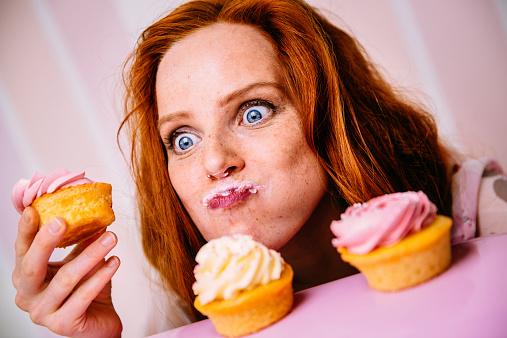 Young red head woman is enjoying cupcakes with a lot of enthusiasm