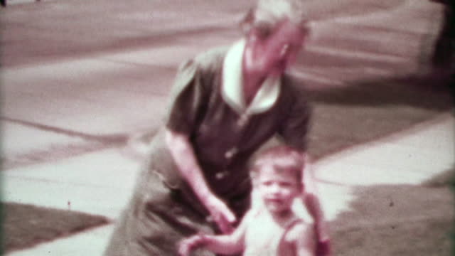 1937: Grandma walking suburban toddler boy as classic cars drive by.