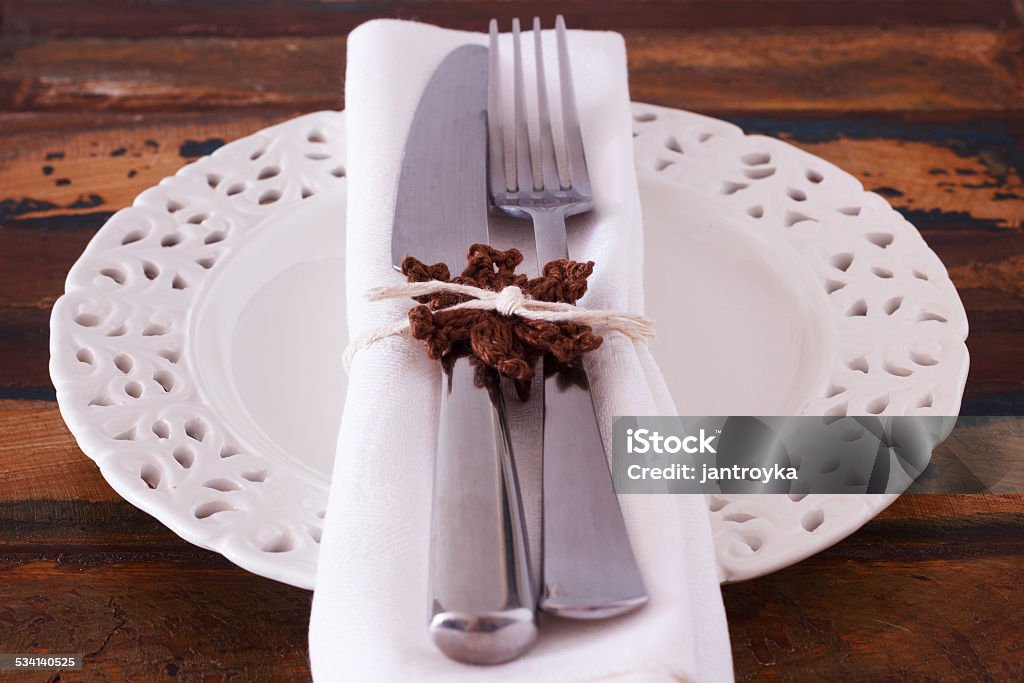 Christmas decoration: White plate serviette fork knife with hand Christmas decoration: White plate serviette fork knife with handmade brown crochet snowflake. Selective focus 2015 Stock Photo
