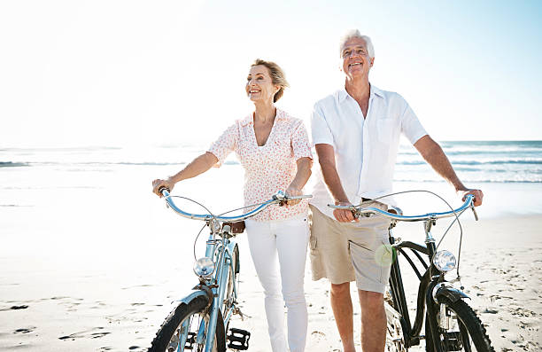 vivez votre vie et oubliez votre âge - senior couple cycling beach bicycle photos et images de collection