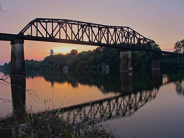 Train Bridge Reflections at Sunset A classic train bridge spans the Black Warrior River at sunset.  alabama stock pictures, royalty-free photos & images