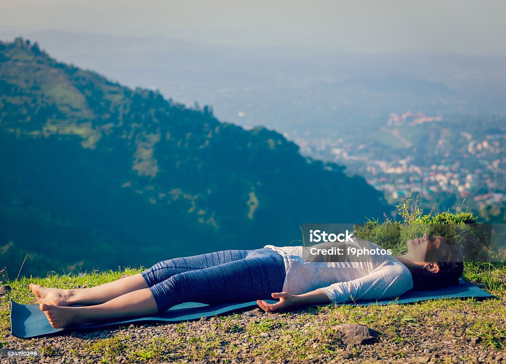 Woman relaxes in yoga asana Savasana outdoors Vintage retro effect hipster style image of woman relaxes in yoga asana Savasana - corpse pose outdoors in Himalayas. Himachal Pradesh, India Shavasana Stock Photo