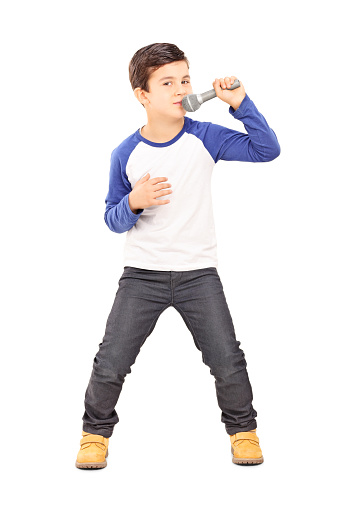 Full length portrait of a joyful little kid singing on a microphone isolated on white background