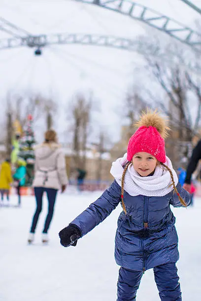 Adorable little girl skating on ice-rink outdoor