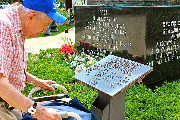 Holocaust Survivor reading dedication plaque at Holocaust Monument Skokie, IL, USA - August 20, 2014: A view of 92 year-old Jewish Holocaust Survivor, Larry Heimlich of Chicago, one of few to survive Nazi Hungarian Arrow Cross slave battalions, reading a dedication plaque at the Holocaust Monument, public art located downtown on the Village Green between Skokie Village Hall and the Skokie Public Library. With the exception of his sister, Eleanor, all the members of his immediate family were murdered at Auschwitz-Birkenau, which included his mother Sari (Sarah), his father Marcus (Meyer), his older brother Herman, sister-in-law Rose, two young nieces and a baby nephew. An annual January 27th International Holocaust Remembrance Day marks the anniversary of the liberation of the Auschwitz-Birkenau death camp in the closing months of World War II. Special memorial ceremonies around the world are planned for the upcoming 70th anniversary of liberation in 2015. holocaust stock pictures, royalty-free photos & images
