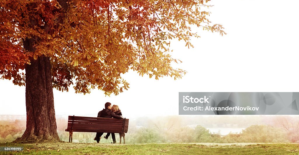 Pareja joven beso en un banco en el gran tema. - Foto de stock de Otoño libre de derechos