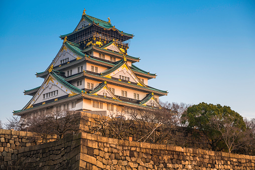 Osaka, Japan - February 26, 2016: The iconic five storey tower of Osaka Castle surrounded by the steep stone walls and tranquil moat of Osaka Castle Park in the heart of downtown Osaka, Japan's vibrant second city. 