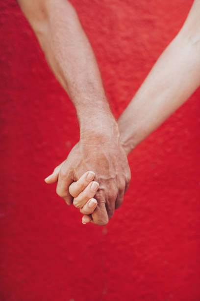 Close up of mature couple holding hands against red wall. Vertical shot of loving man and woman holding hands.