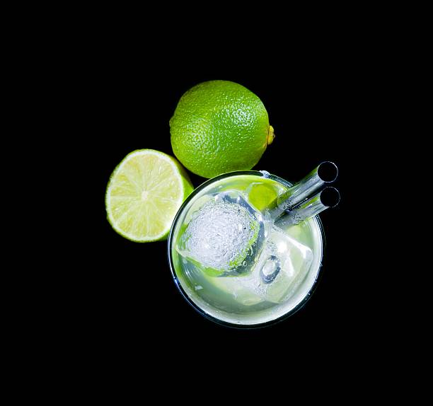 glasses with cocktail and ice near lime on black background