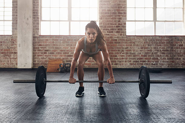 Female performing deadlift exercise with weight bar Female performing deadlift exercise with weight bar. Confident young woman doing weight lifting workout at gym. weight training stock pictures, royalty-free photos & images
