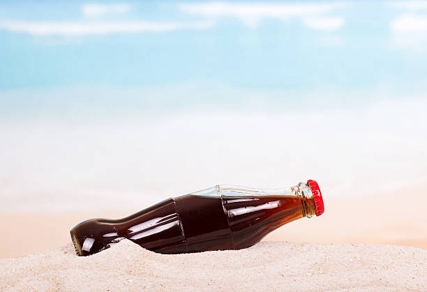 A bottle of cola in the sand on the seashore.