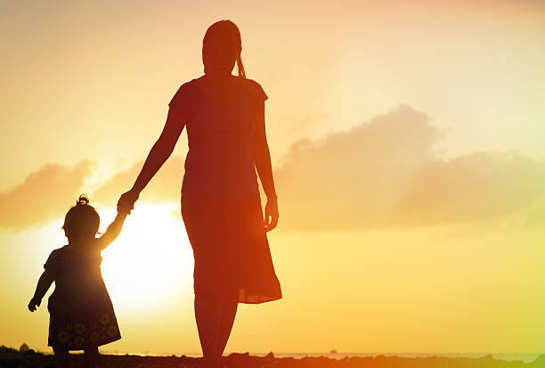 istock mother and little daughter walking on beach at sunset 534217785
