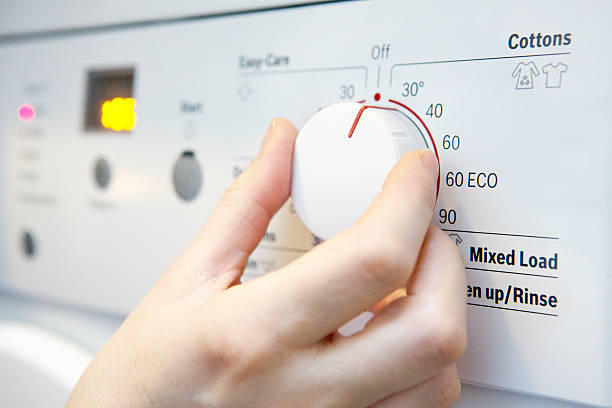 frau auswahl kühleren temperaturen auf waschmaschine, um energie zu sparen - waschmaschine stock-fotos und bilder
