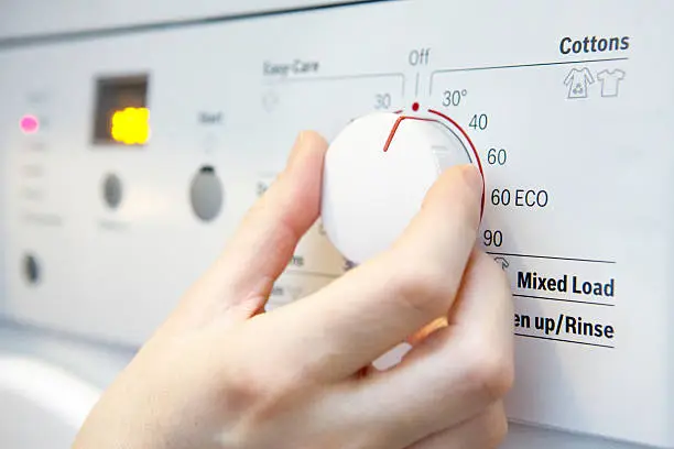 Woman Selecting Cooler Temperature On Washing Machine To Save Energy