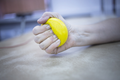 Female patient with physical injury and Rheumatoid arthritis squeezing physiotherapy ball with hand in hospital clinic resting on bed.
