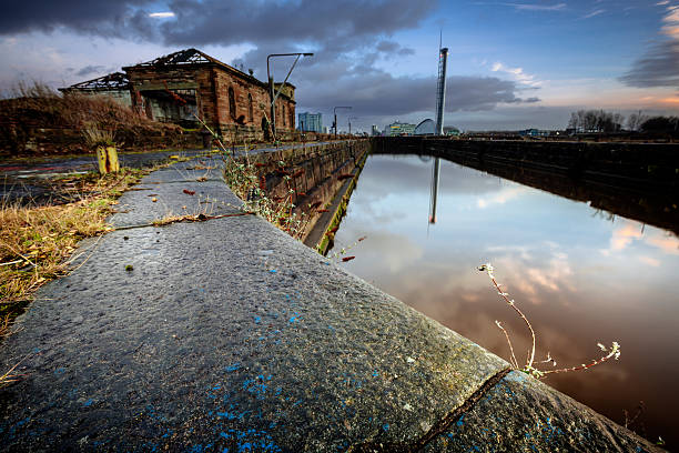 The Derelict Graving Docks at Govan Burnt out buildings amongst the overgrowth at the derelict Victorian graving docks - a type of dry dock - in Govan, Glasgow, on the River Clyde at sunset. In the background is the modern Glasgow skyline. govan stock pictures, royalty-free photos & images