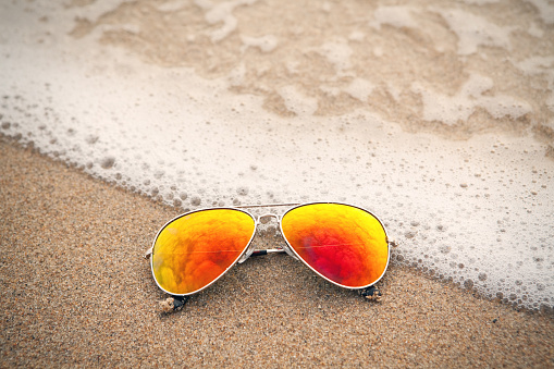 Mirrored sunglasses laying on a beach reflecting the overcast skies above.