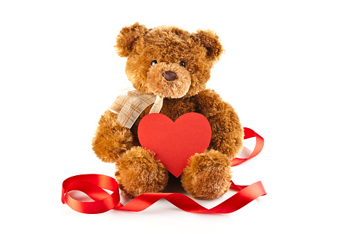 Teddy Bear is sitting on white background holding red heart shaped blank card and surround by a red ribbon
