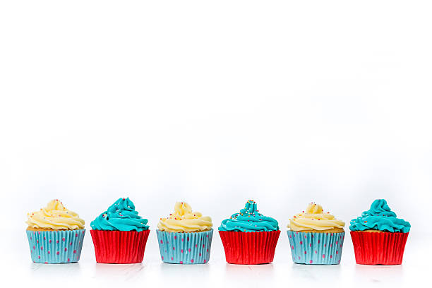 Selection of six tasty looking cupcakes in vivid blue, red and butter cream colours insulated on white background. Aligned at the bottom of the frame to allow copy space. Indoors studio shot with Canon EOS.