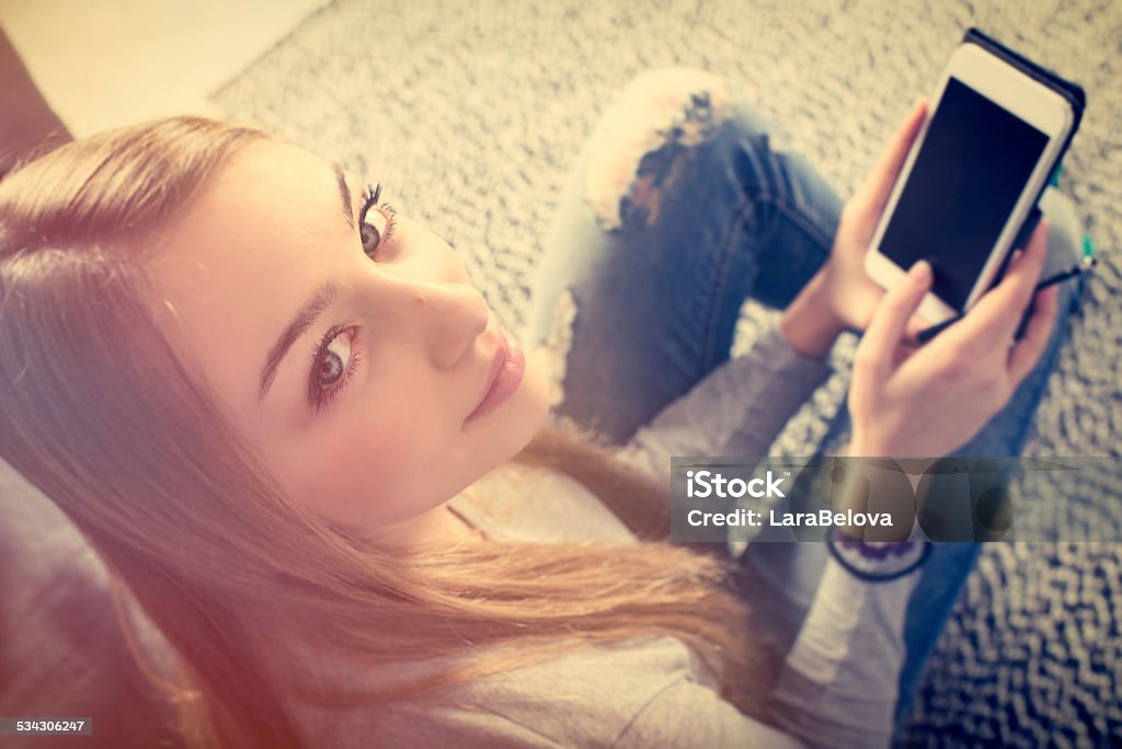Teenage girl with smart device Teenage girl with smart device in domestic room. 18-19 Years Stock Photo