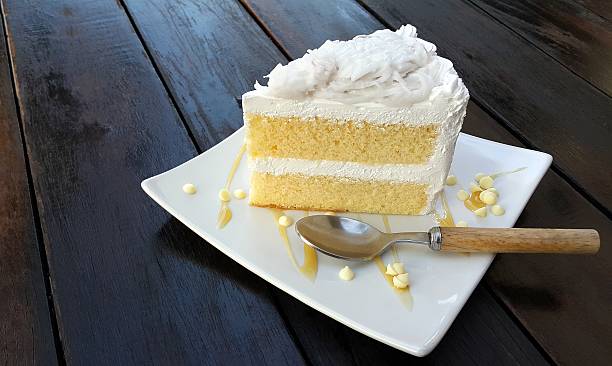 Piece of coconut cake on white plate with spoon stock photo