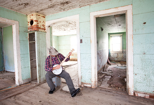 A banjo picker playing bluegrass music in an old abandoned house. Caucasian male in his 40s