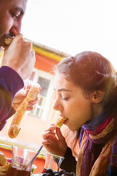 Young Turkish couple enjoying simit sesame bagels and tea on their balcony. Lens flare, Autumn clothing.