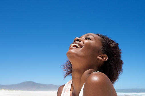Close up portrait of beautiful young african woman laughing outdoors against sky