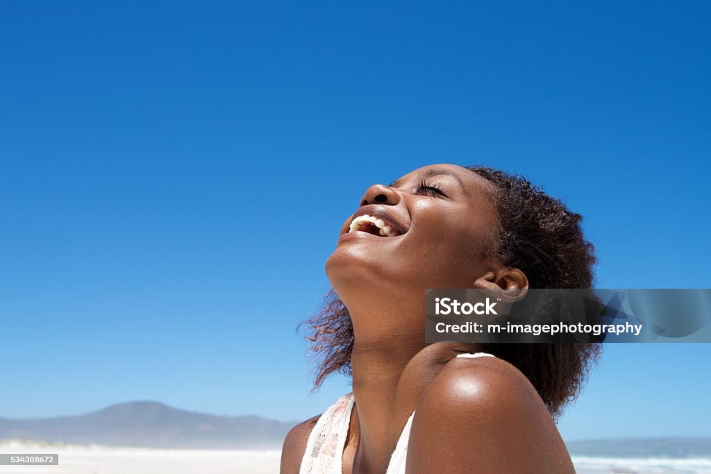 Beautiful young african woman laughing outdoors Close up portrait of beautiful young african woman laughing outdoors against sky Women Stock Photo