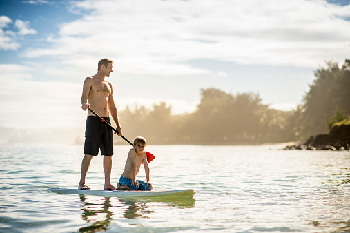 Father and son in Hawaii's tropical climate enjoying their vacation on stand up paddleboards (SUP) in the sea.