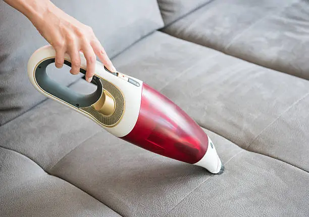 Natural female hands cleaning the sofa couch with a handheld vacuum cleaner
