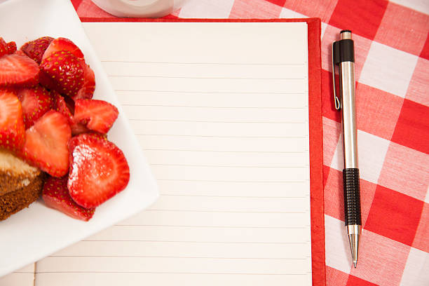 Fresh strawberry fruits on plate. Notepad, pen.