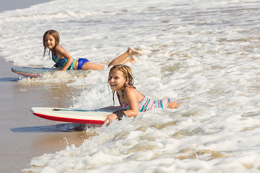 Cute little girls boogie boarding in the ocean waves