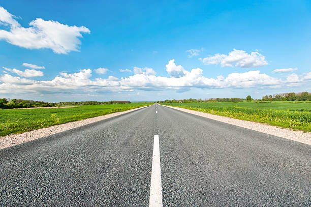 asphalt road in green fields on blue cloudy sky background - weg stockfoto's en -beelden