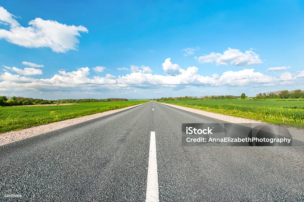 Asphalt road in green fields on blue cloudy sky background Asphalt road in green fields on blue cloudy sky background. Multicolored vibrant outdoors horizontal image. Road Stock Photo