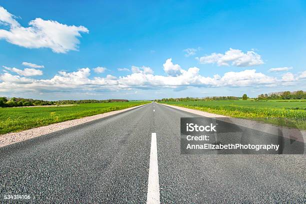 Asphalt Road In Green Fields On Blue Cloudy Sky Background Stock Photo - Download Image Now