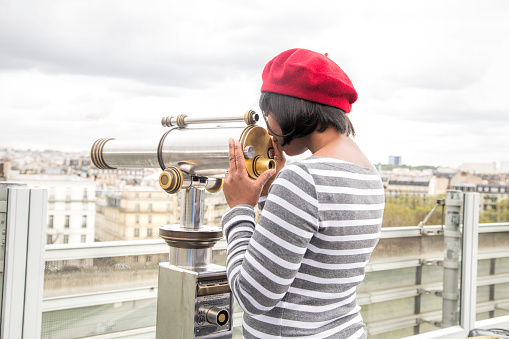 Tourist of African decent looking at Paris through telescope.