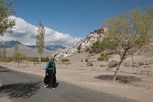 Thikse, India - May 12th, 2009: Unidentified Ladakhi woman walks after visiting a puja on the background of Buddhist monastery in Thikse, Ladakh, India on May 12, 2009.