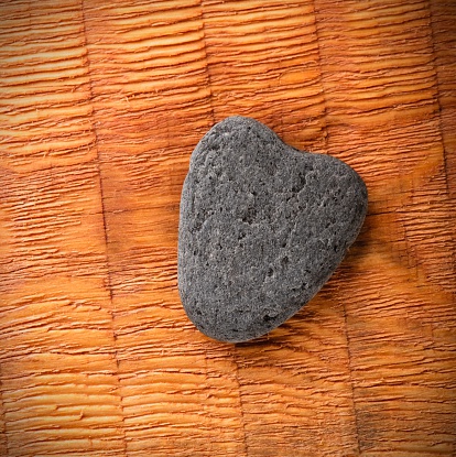 Square photo of slate grey stone with shape of heart. Heart shaped stone placed on wooden board with parallel grooves. Corners with visible vignetting.