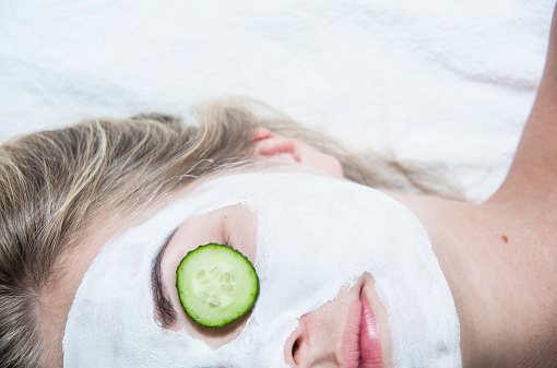 Young woman with clay facial mask in spa salon, closeup portrait, half face