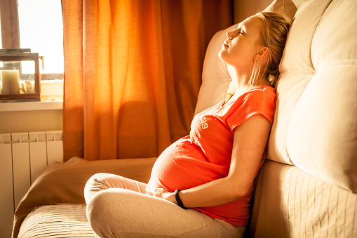 Young pregnant woman with closed eyes relaxing. Warm sunlight falls from the window on women face