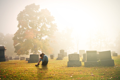 A woman in mourning sitting ina cemetery in the early morning.