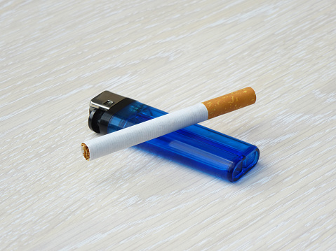 Lighter with cigarette on top laying flat on a wooden  surface.